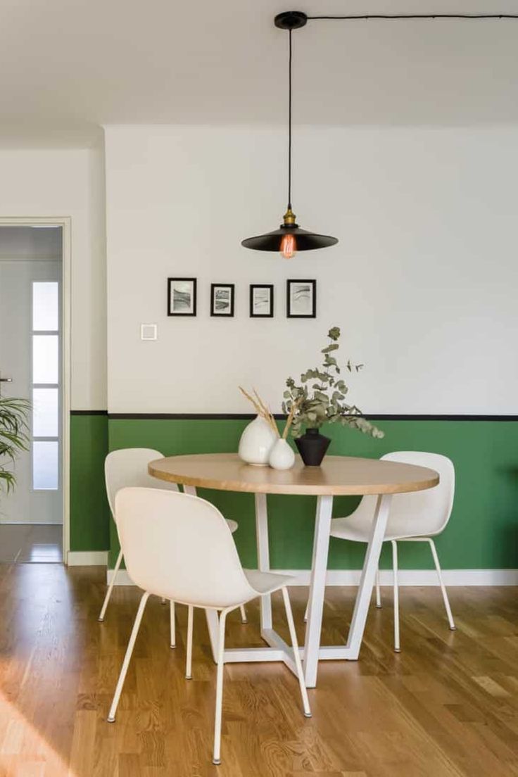 a dining room table with white chairs next to a green wall and potted plant