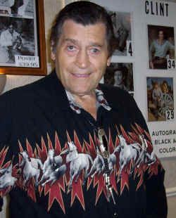 a man in a black and red shirt standing next to a wall with pictures on it