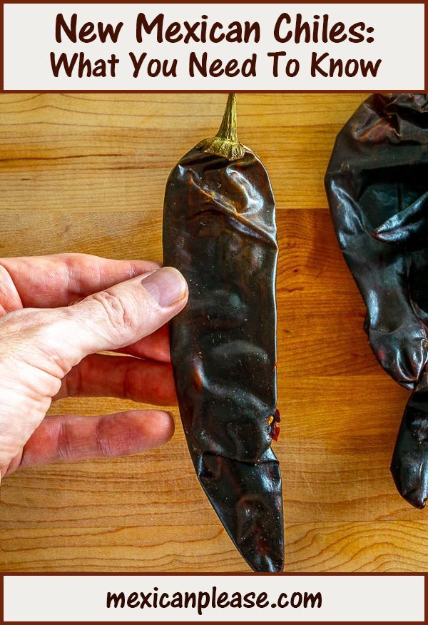 a hand reaching for a mexican chilli pepper on a wooden table with text overlay that reads, new mexican chiles what you need to know