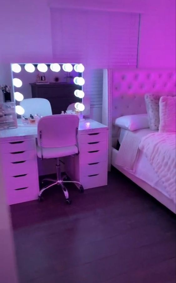 a bedroom with a bed, desk and mirror in the room that has lights on