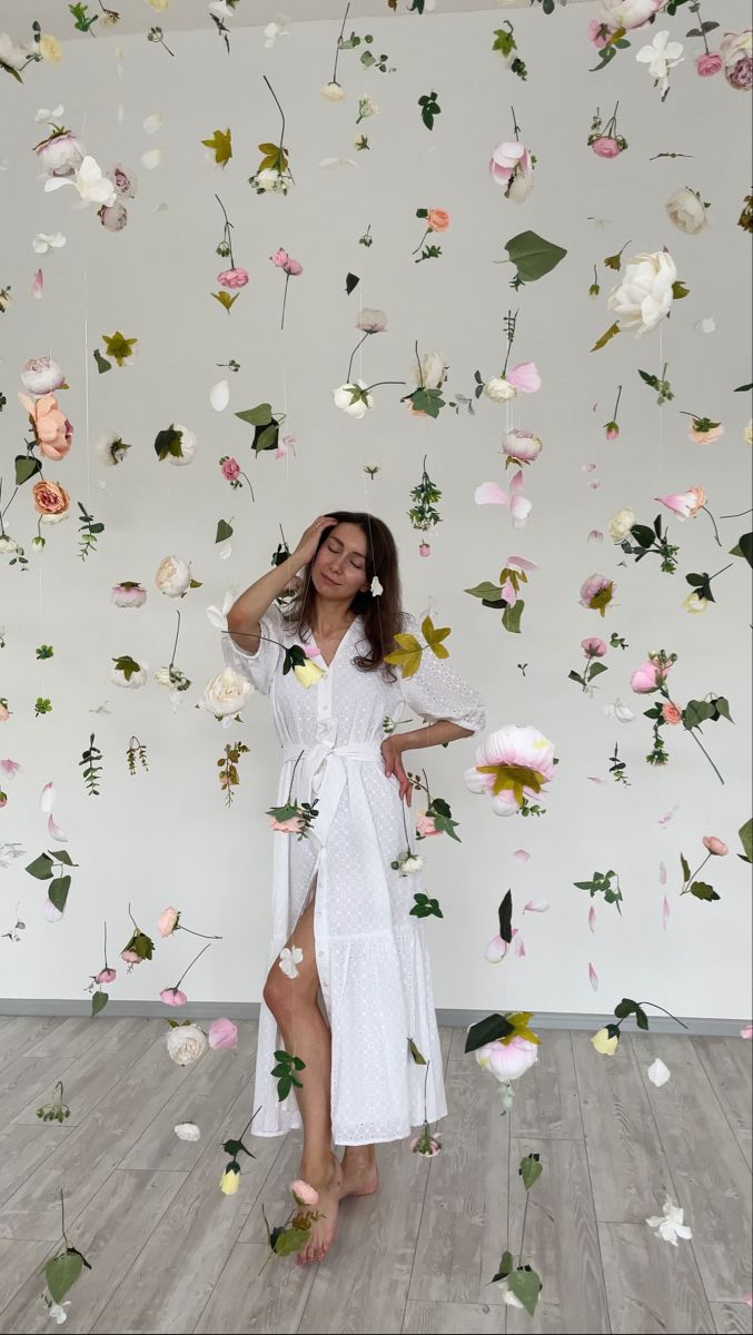 a woman standing in front of a wall with flowers all over it and one leg on the floor