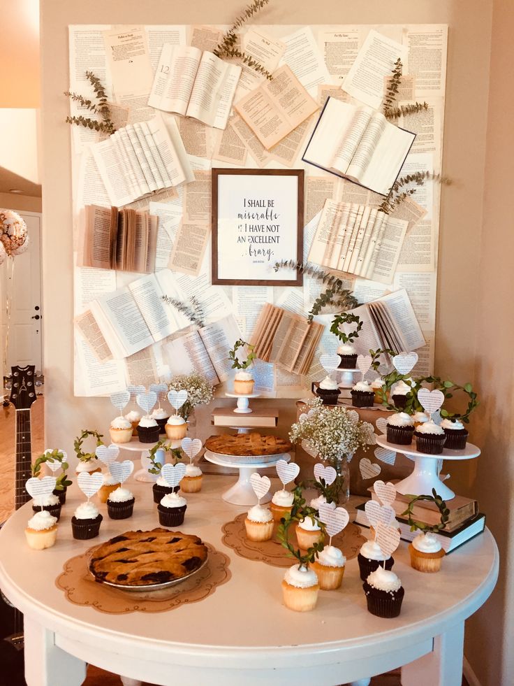 a table topped with cupcakes covered in frosting next to an open book