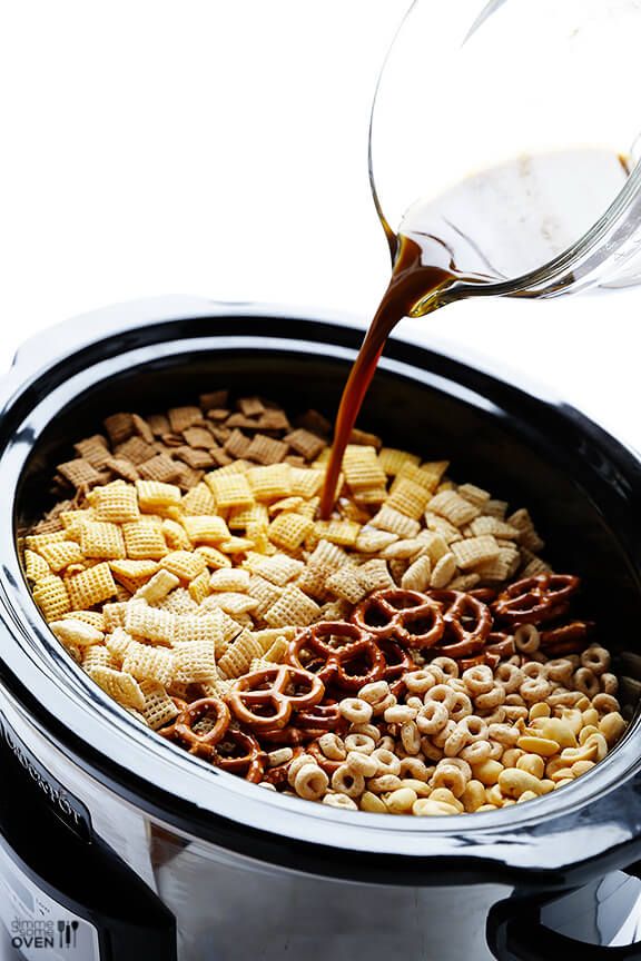 a person pouring some liquid into a crock pot filled with cheesy crackers