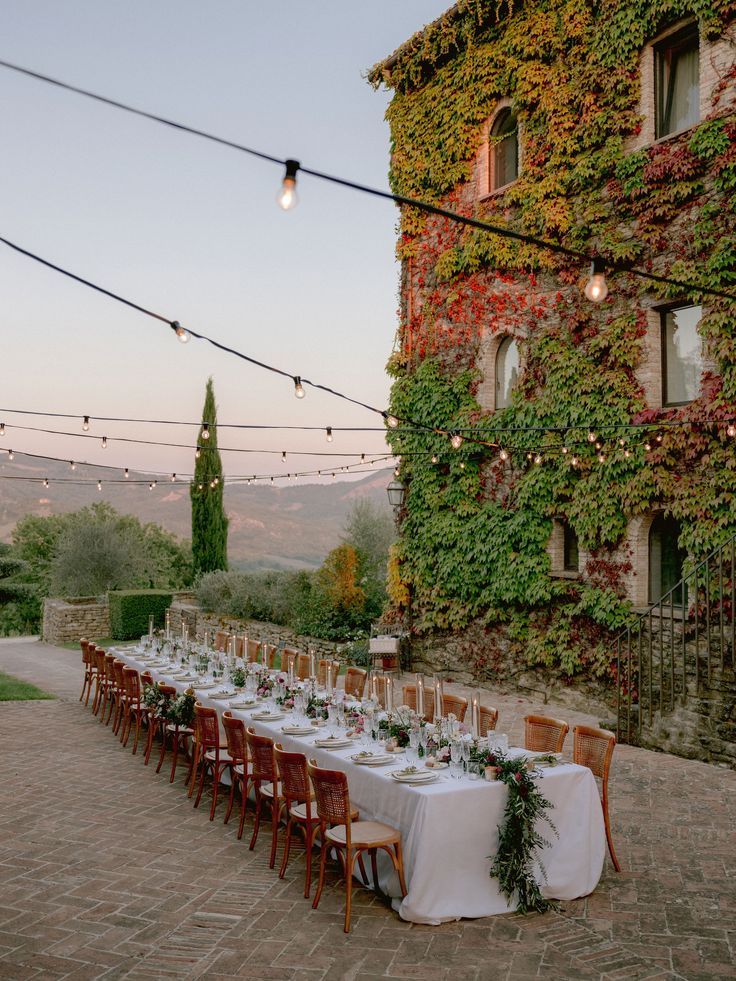 an outdoor dining area with long tables and chairs set up for dinner outside at dusk