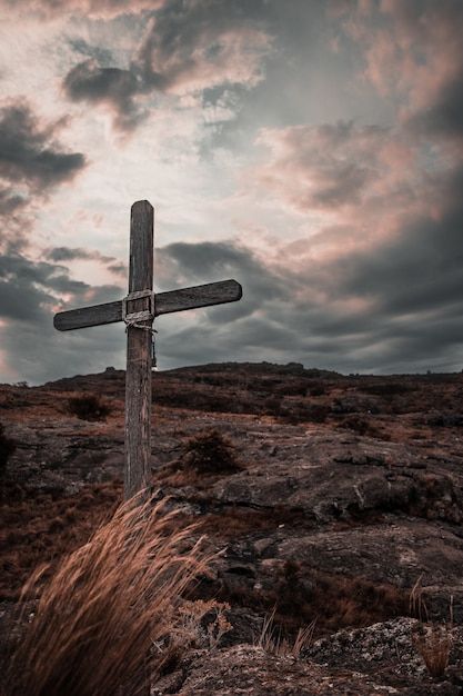 a wooden cross sitting on top of a dry grass covered hill under a cloudy sky