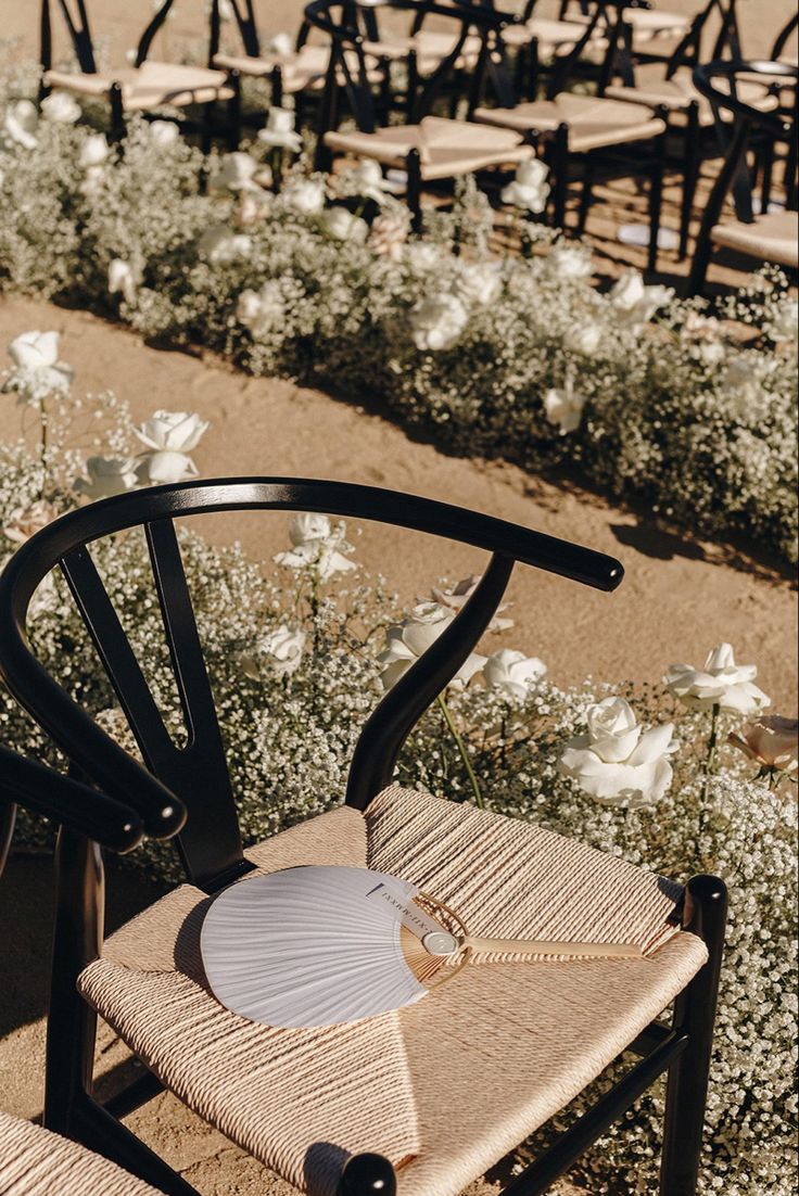 an empty chair sitting in the middle of a field with white flowers and chairs behind it