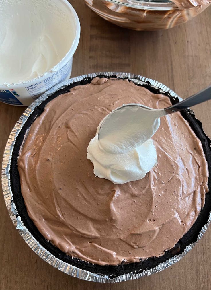 a chocolate pie with whipped cream on top and another pie in the background, ready to be eaten