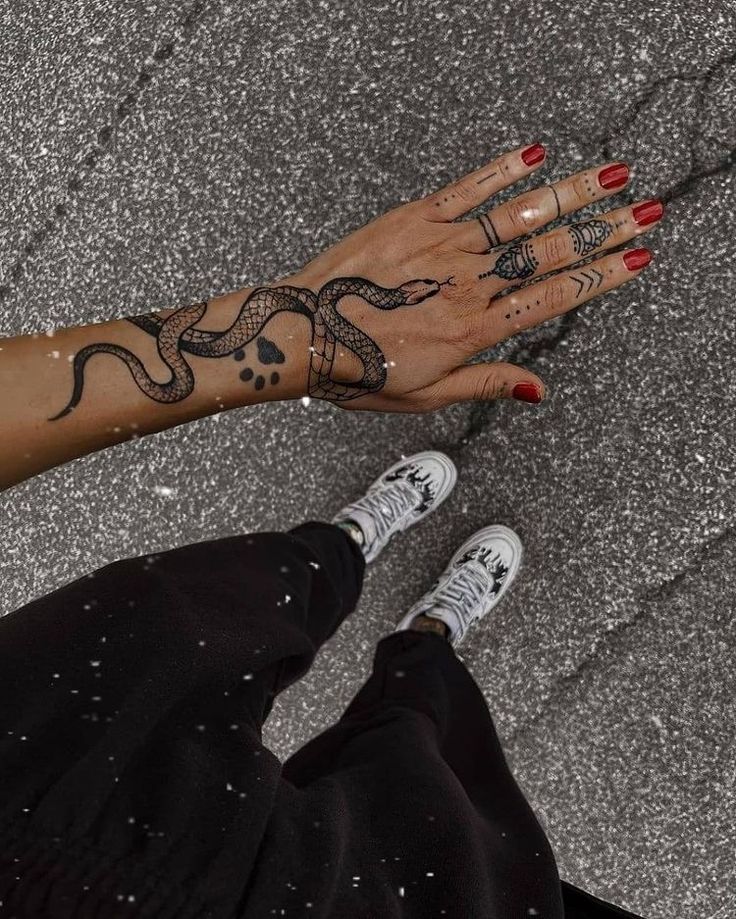 a woman's hand with a snake tattoo on her left arm and right hand