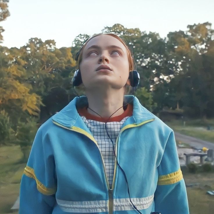 a young woman wearing headphones looking up at the sky with trees in the background