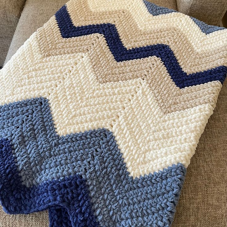 a blue and white crocheted blanket sitting on top of a couch next to a pillow