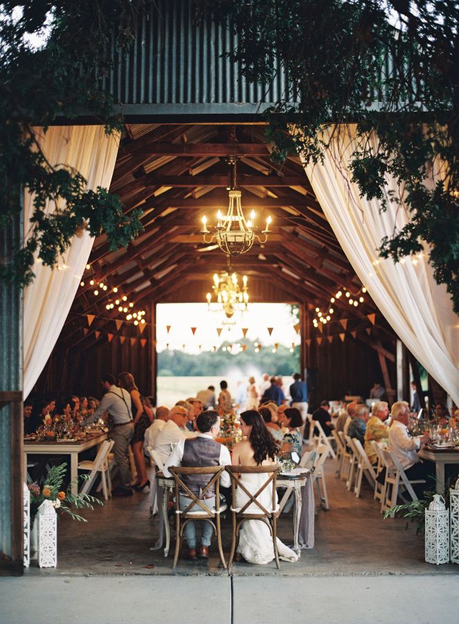 a group of people sitting at tables under a wooden structure with white draping