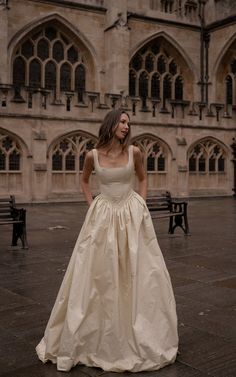 a woman standing in front of a building wearing a wedding dress and looking at the camera