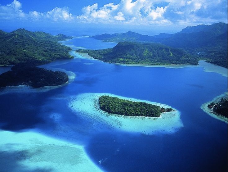 an aerial view of several small islands in the water with blue sky and clouds above them