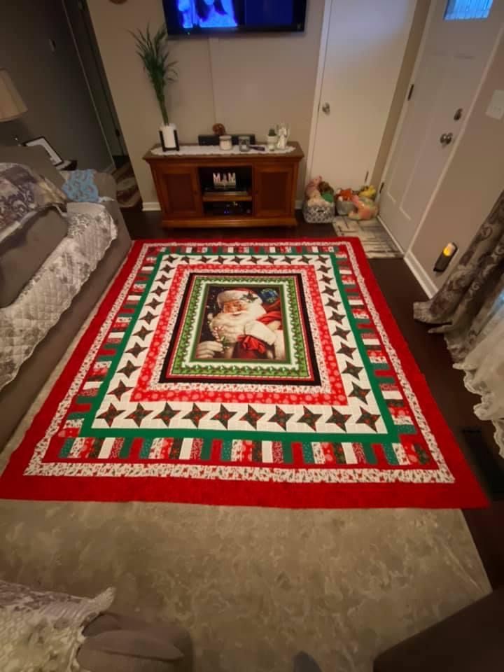 a christmas quilt on the floor in front of a flat screen tv with santa claus