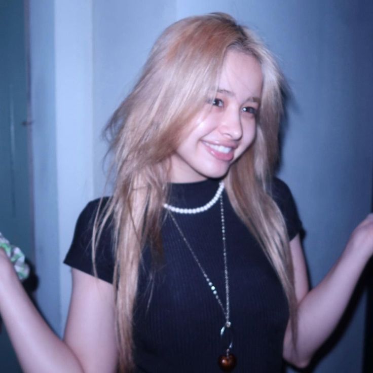 a woman with long blonde hair wearing a black shirt and holding something in her hand