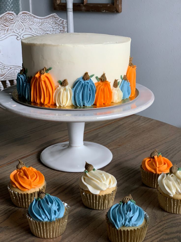 there are cupcakes on the table with frosting and pumpkins around them