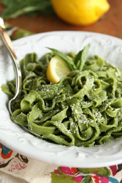 a white bowl filled with green pasta on top of a table next to lemons