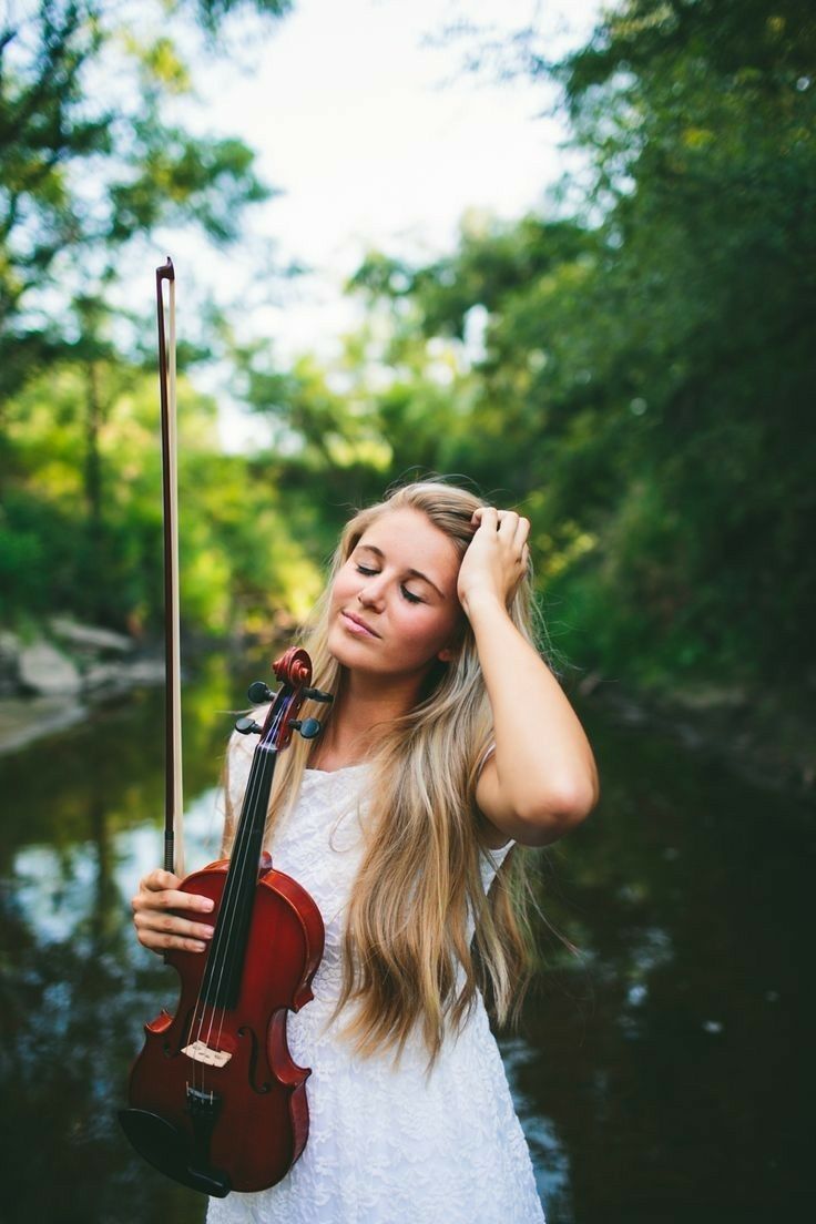 a young woman holding a violin in her right hand while standing next to a river