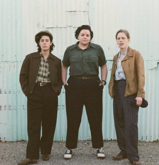 three women standing next to each other in front of a metal building with a blue wall behind them