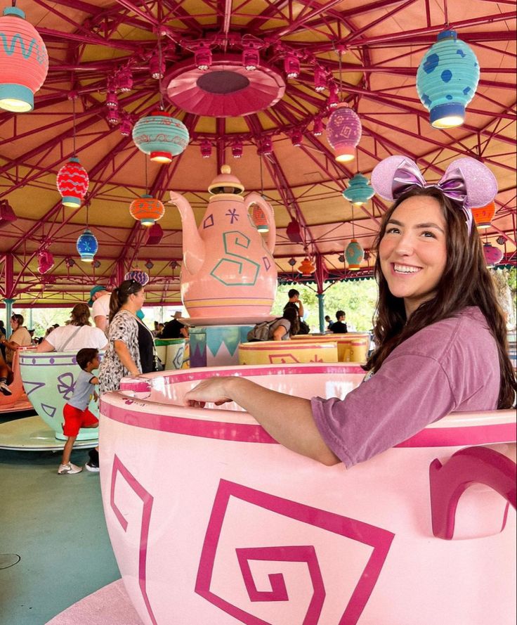 a woman is sitting in a pink and white toy car at an amusement park with lots of decorations