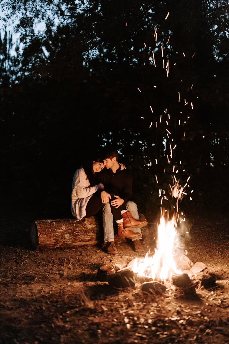 two people sitting next to a campfire at night with sparklers in the air