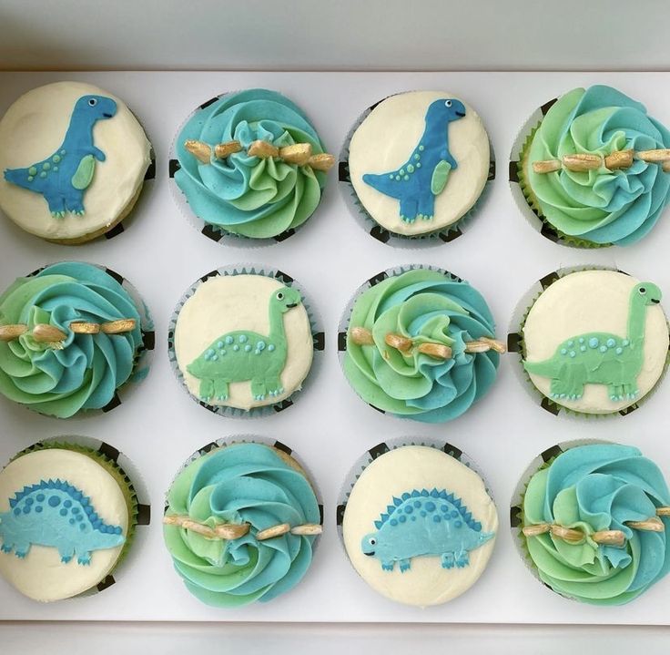 twelve cupcakes decorated with blue and green frosting, including one dinosaur design