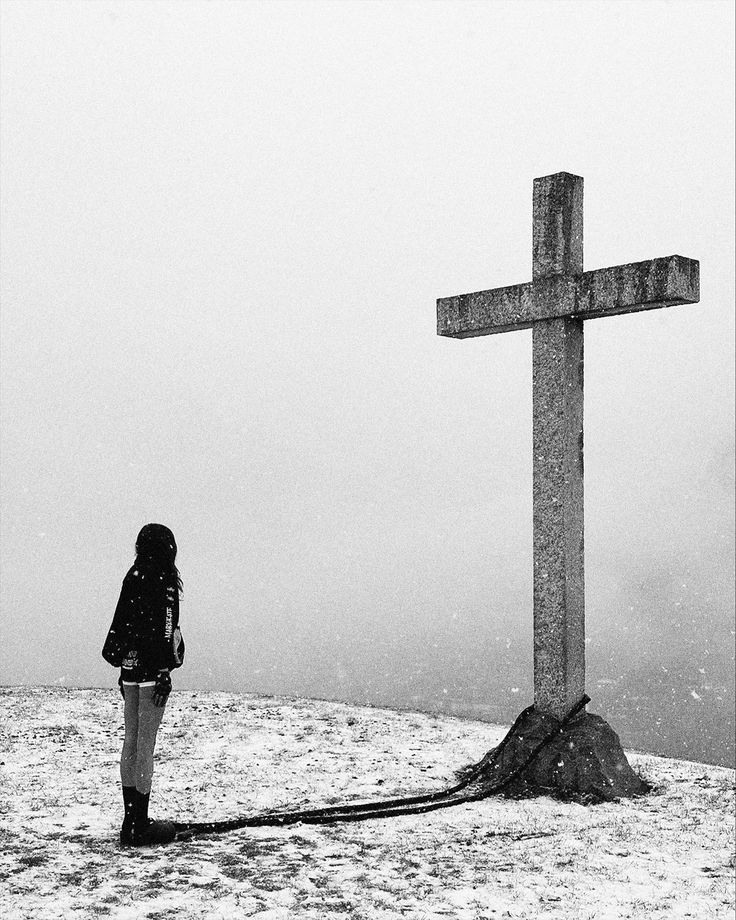 a woman standing in front of a cross on top of a snow covered hill