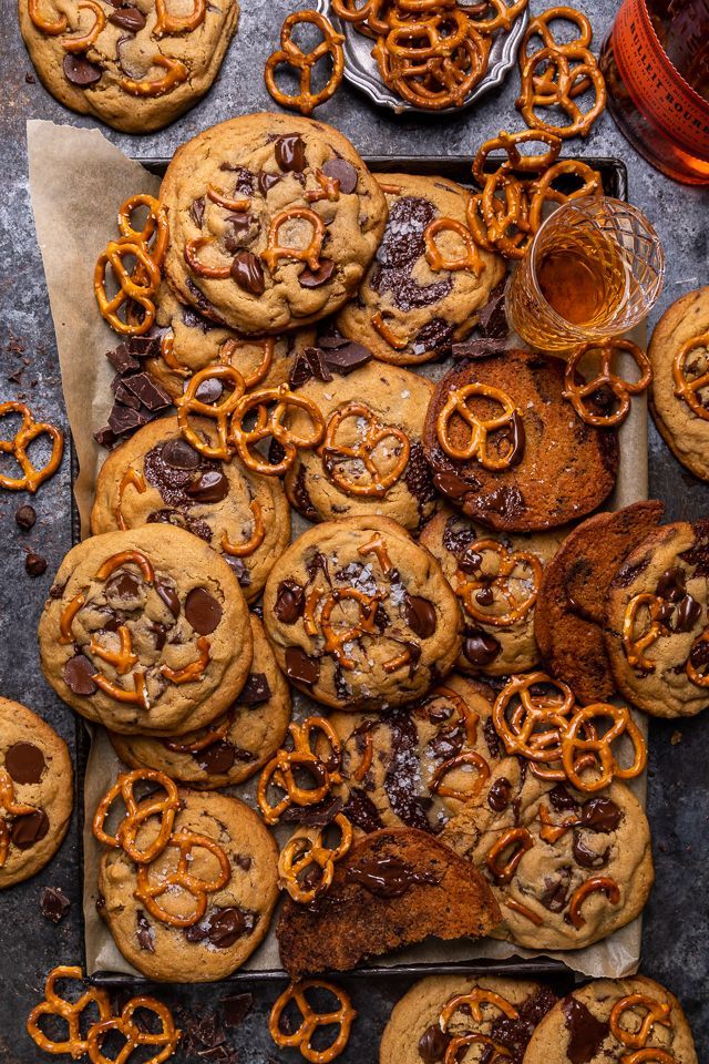 chocolate chip cookies and pretzels are arranged on top of parchment paper, next to a glass of beer