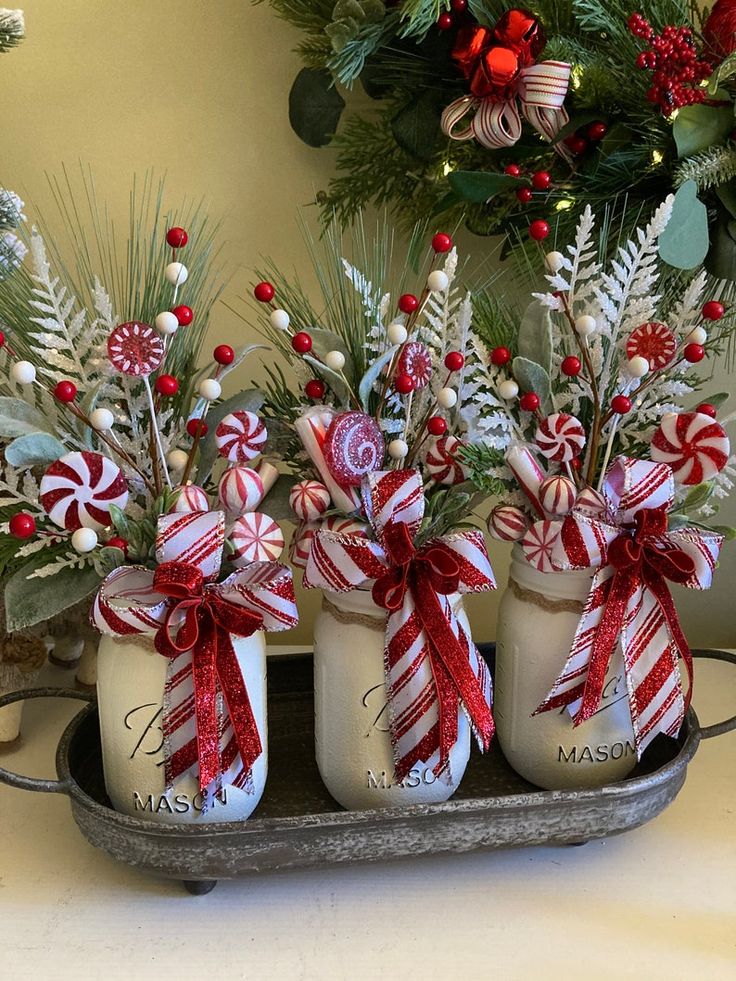 three mason jars filled with candy canes and greenery are sitting on a tray