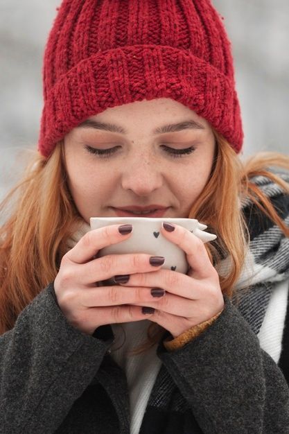 a woman with red hair is holding a cup and looking at her cell phone in the snow