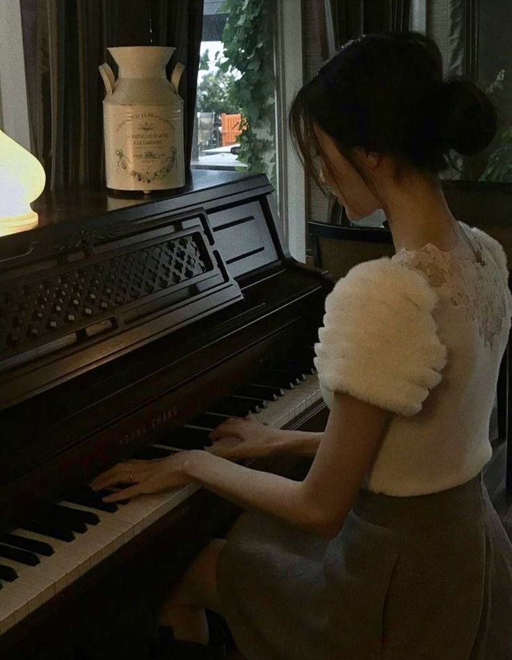 a woman sitting at a piano in front of a window