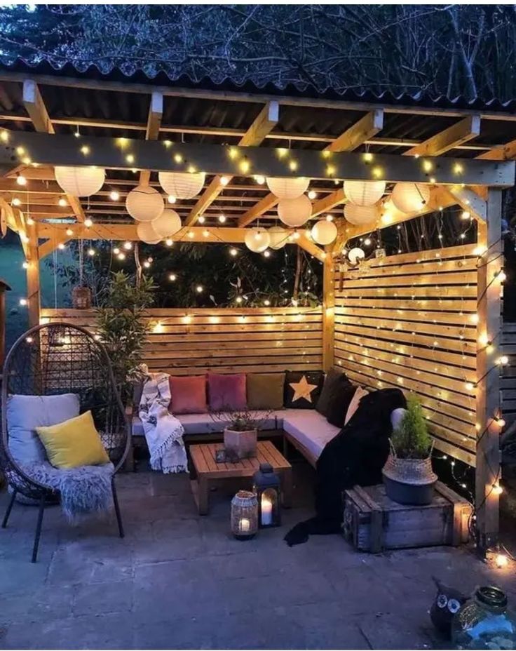 an outdoor seating area with lights on the ceiling and wooden slatted walls behind it