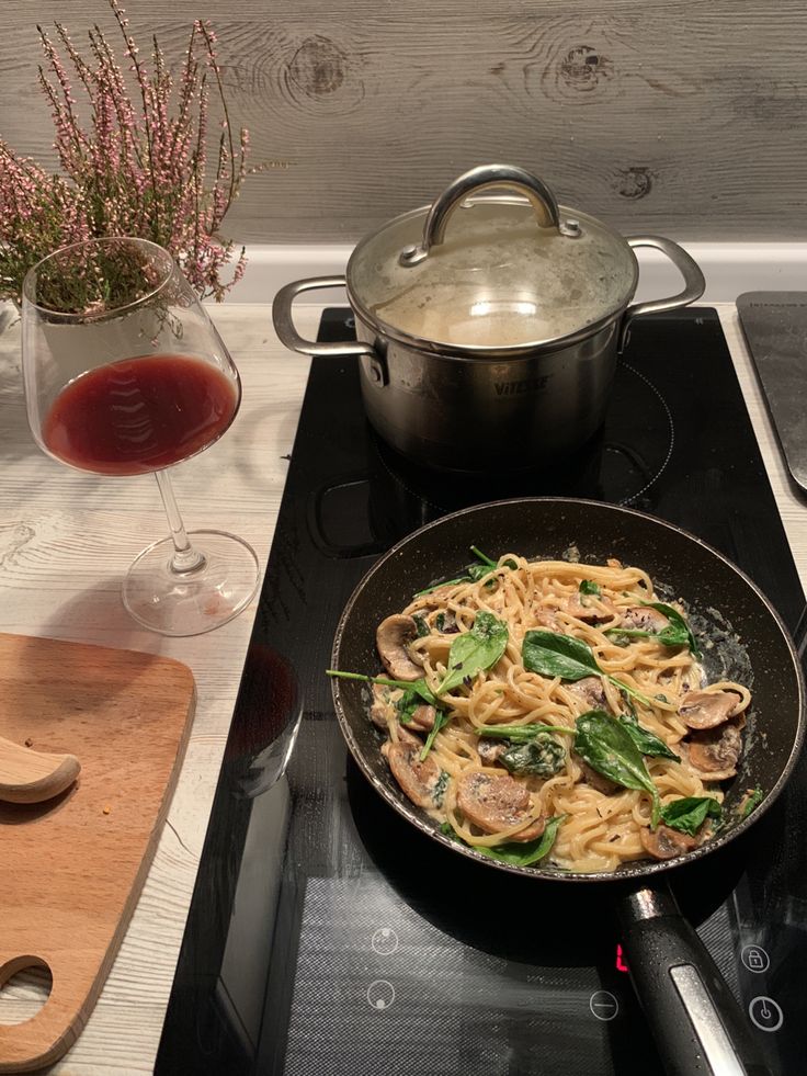 a skillet with pasta and vegetables on the stove next to a glass of wine