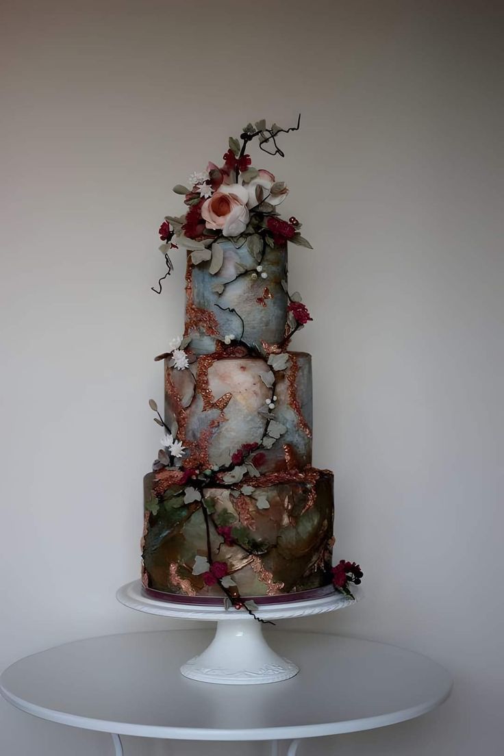 a multi - tiered cake with flowers on top sits on a white table in front of a wall