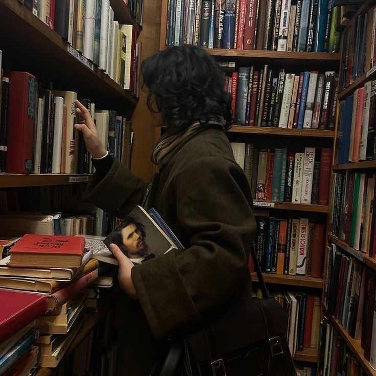 a woman standing in front of a bookshelf holding a book and looking at it