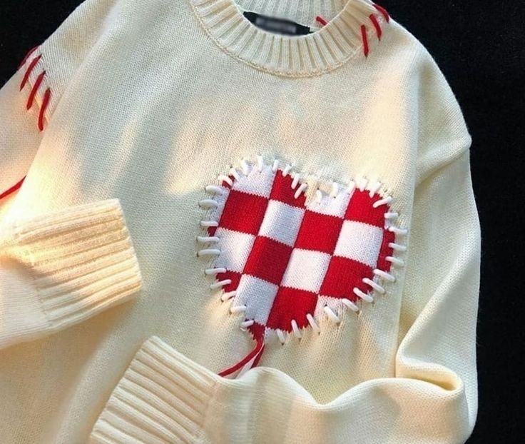 a white sweater with a red and white heart on the front, next to a pair of gloves