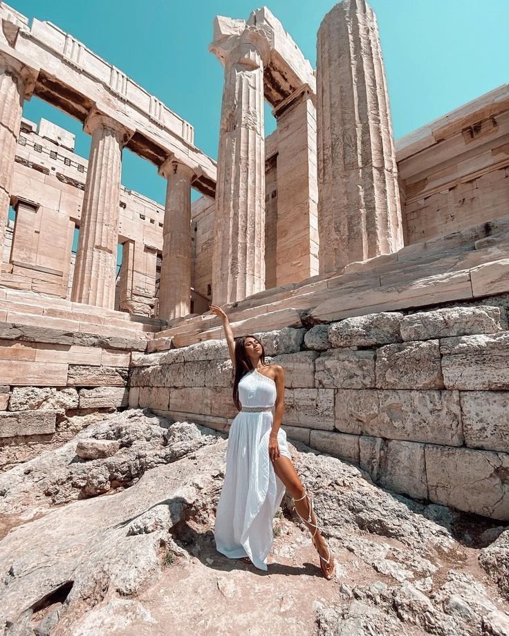 a woman standing on top of a rock next to some stone pillars in front of an ancient building