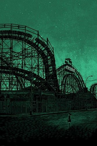 the roller coaster is lit up green in this dark night time scene with a person walking by