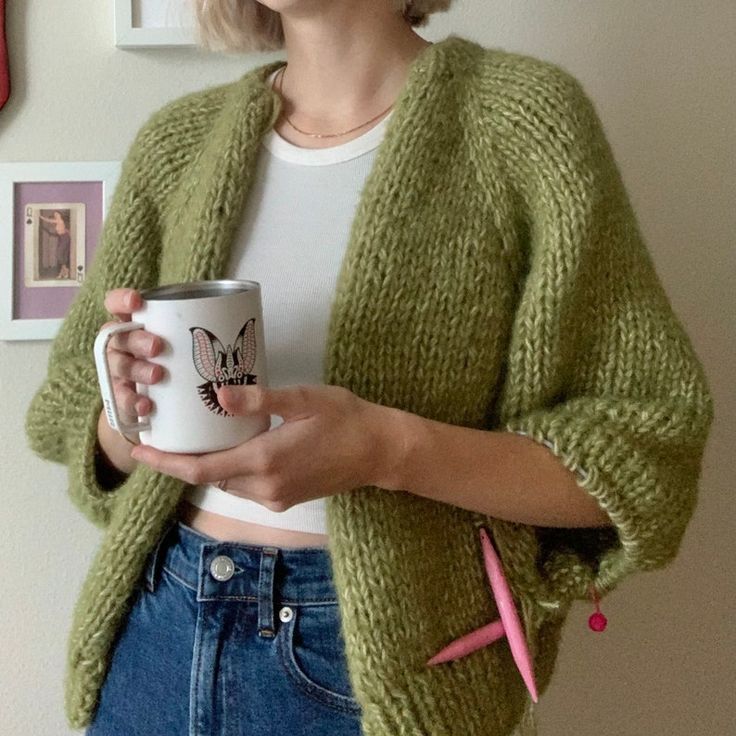 a woman is holding a coffee mug in her right hand and wearing a green cardigan