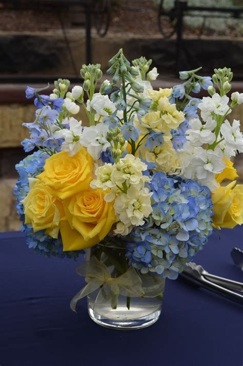 a vase filled with yellow and blue flowers on top of a table next to silverware