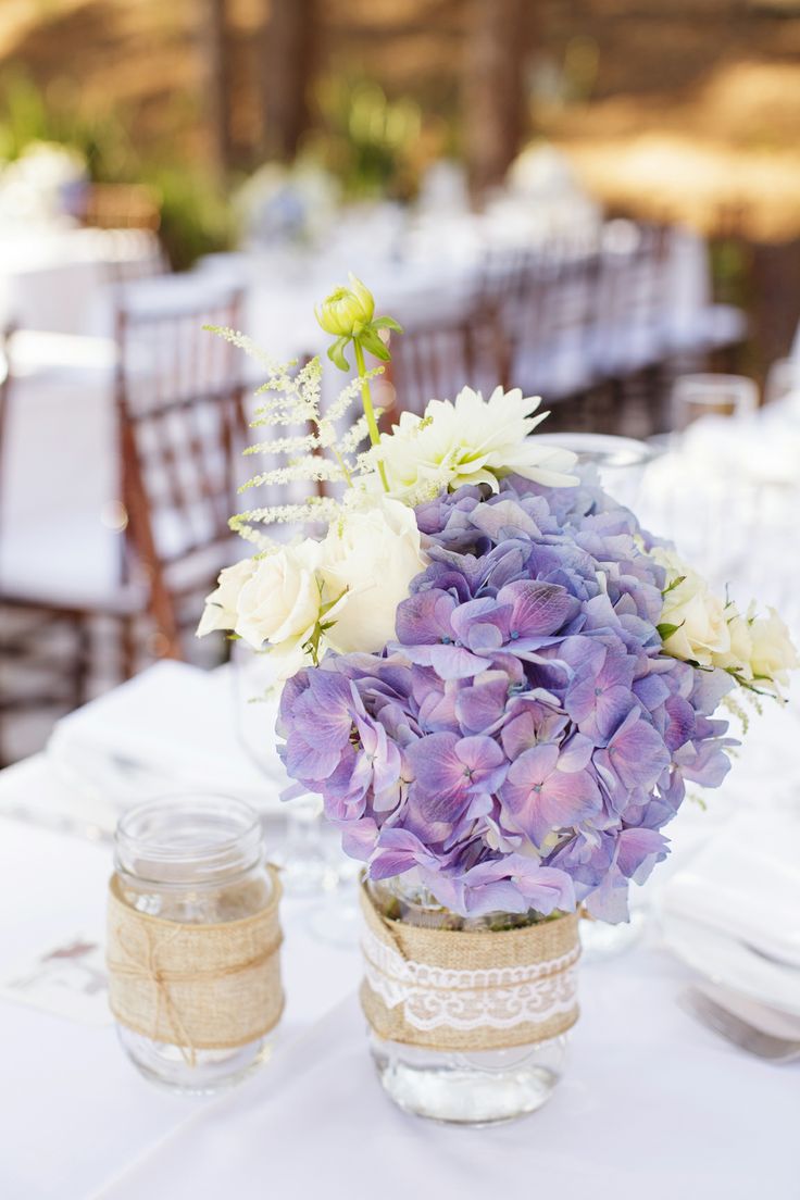 a vase filled with purple and white flowers sitting on top of a table next to a mason jar