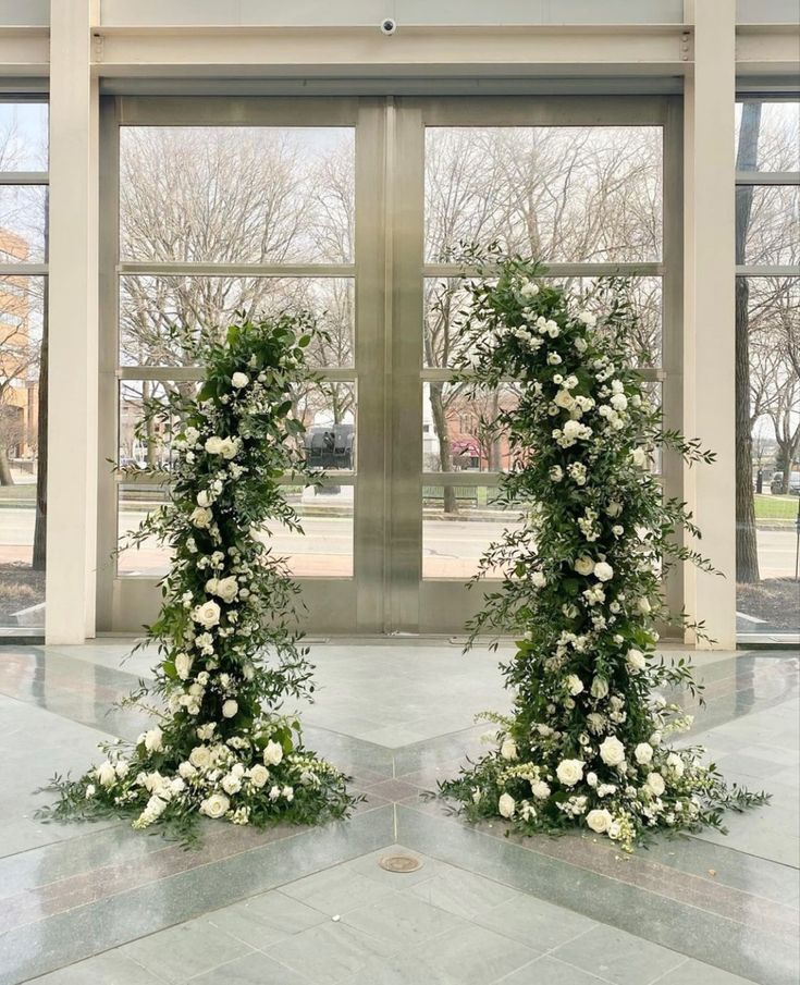 two white flowers are on display in front of large windows