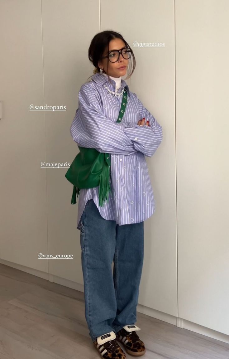 a woman standing in front of a white wall wearing glasses and a green scarf around her neck