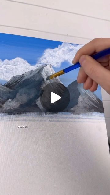 a person is holding a pencil and painting mountains