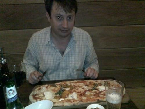 a man sitting at a table with a pizza in front of him