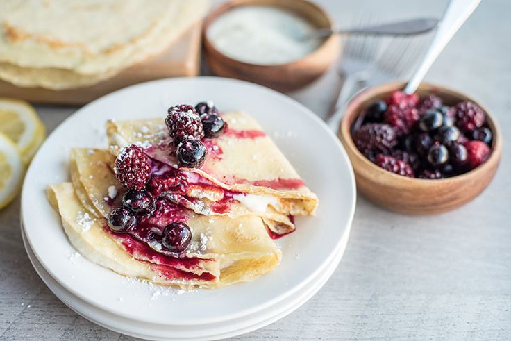 crepes with berries and powdered sugar sit on a plate next to lemon slices