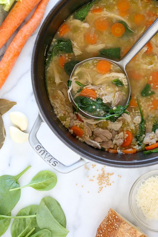 a pot full of soup with carrots, spinach and parmesan cheese