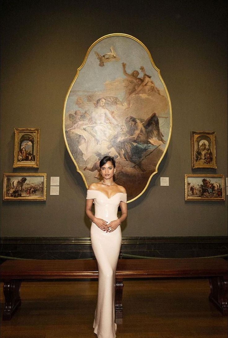 a woman in a white dress standing next to a wall with paintings on the walls