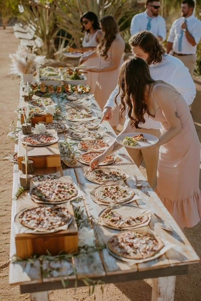 people are standing around a long table with pizzas on it and plates in front of them