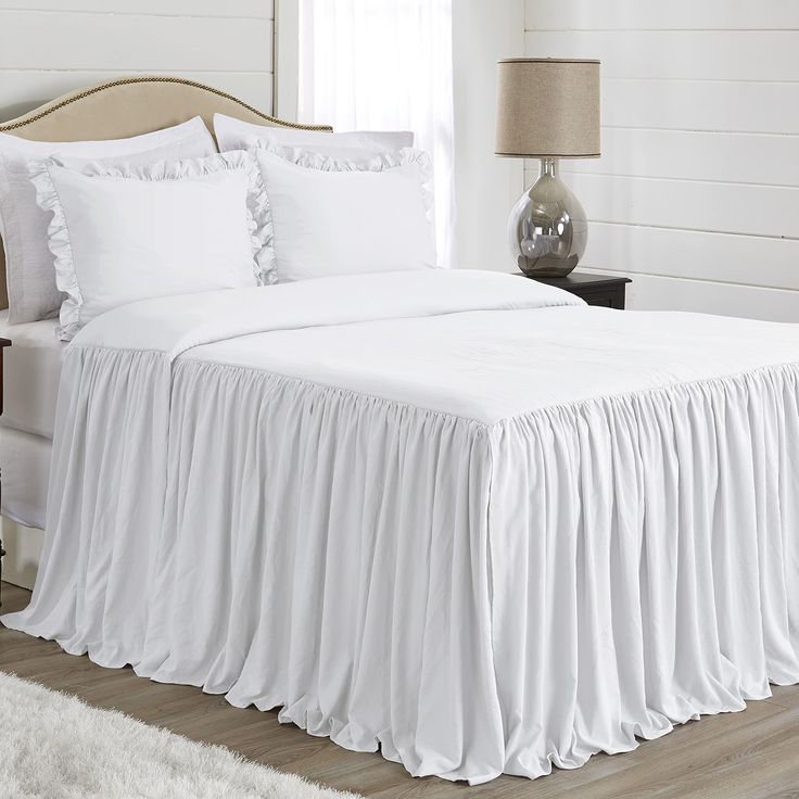 a white bed with ruffled bedspread and pillows